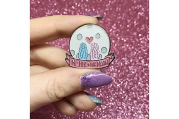 moon shaped enamel pin with two figures viewed from the back and the words me her and the moon
